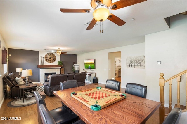 dining space featuring a tiled fireplace, a ceiling fan, wood finished floors, baseboards, and stairs