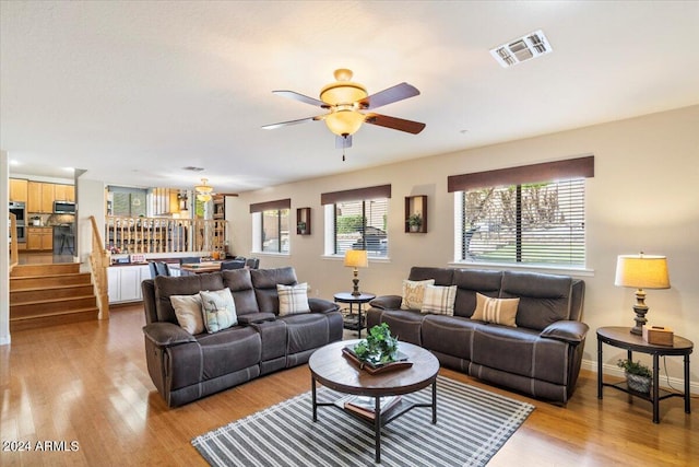 living area featuring light wood finished floors, baseboards, visible vents, a ceiling fan, and stairway