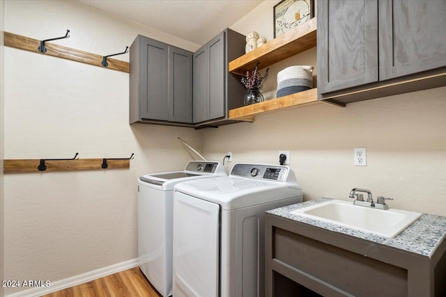 laundry area with cabinets, separate washer and dryer, sink, and light hardwood / wood-style floors