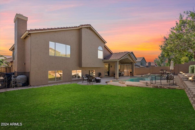 back house at dusk with a fenced in pool, a lawn, and a patio area