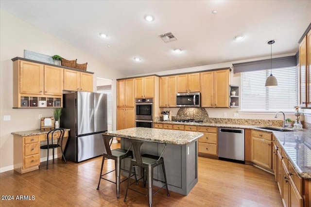 kitchen with sink, appliances with stainless steel finishes, light stone counters, a kitchen island, and decorative light fixtures