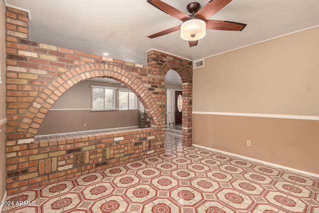 unfurnished living room featuring ceiling fan and brick wall