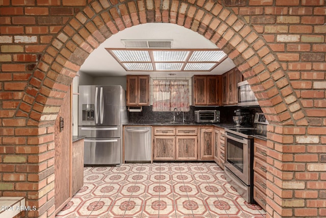 kitchen featuring sink, stainless steel appliances, brick wall, dark stone countertops, and decorative backsplash