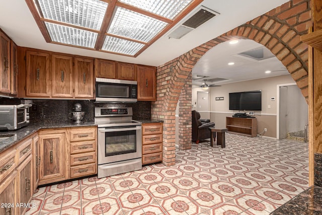 kitchen with appliances with stainless steel finishes, tasteful backsplash, ceiling fan, and dark stone counters