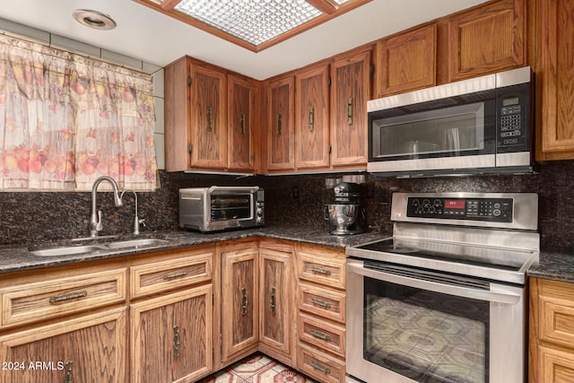 kitchen with tasteful backsplash, stainless steel appliances, sink, light tile patterned floors, and dark stone countertops