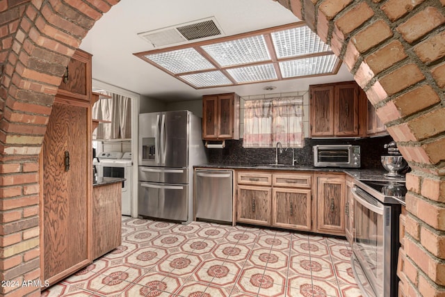 kitchen with sink, stainless steel appliances, backsplash, dark stone counters, and washer and dryer