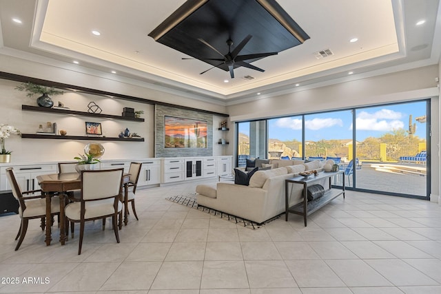 living area with light tile patterned floors, visible vents, a raised ceiling, and ceiling fan