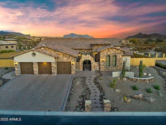 view of front of property with an attached garage, a tile roof, decorative driveway, stone siding, and a mountain view