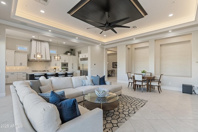 living area with light tile patterned floors, visible vents, a raised ceiling, and baseboards