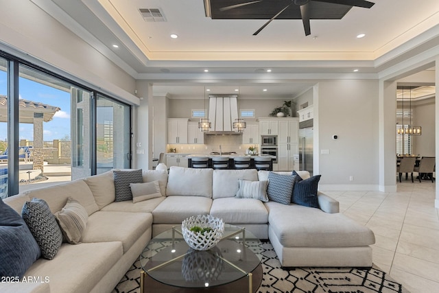 living area with visible vents, ceiling fan with notable chandelier, a tray ceiling, light tile patterned flooring, and crown molding