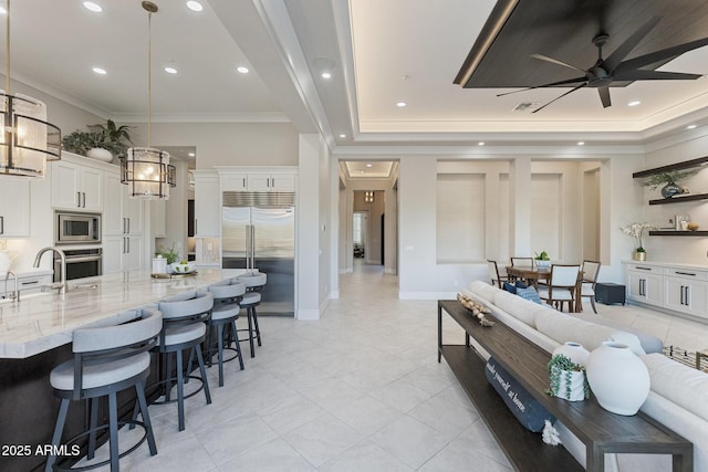 kitchen featuring light stone countertops, white cabinets, built in appliances, a kitchen bar, and crown molding