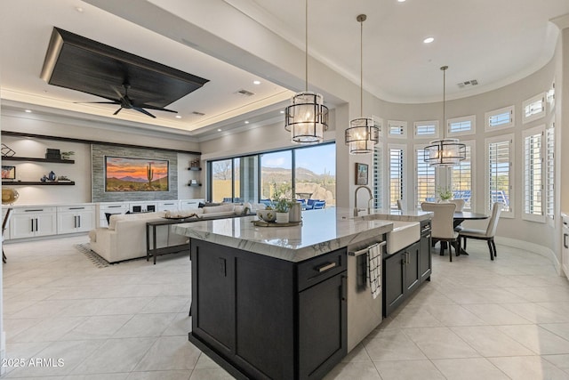 kitchen with a tray ceiling, visible vents, dark cabinets, and a sink