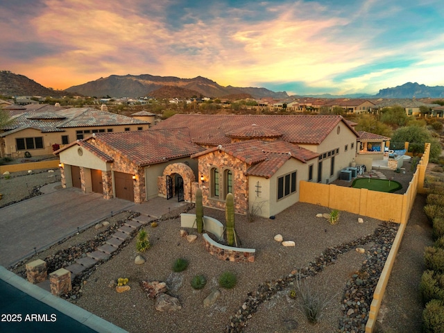 mediterranean / spanish-style home featuring a fenced backyard, a garage, stone siding, a tile roof, and a mountain view