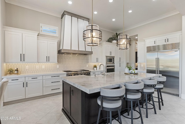 kitchen featuring crown molding, backsplash, a kitchen island with sink, and built in appliances