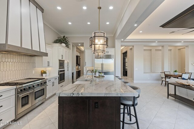 kitchen with wall chimney range hood, built in appliances, a breakfast bar, ornamental molding, and a sink