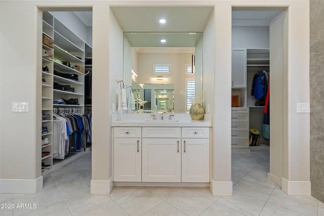 bathroom with tile patterned flooring, vanity, a walk in closet, and baseboards