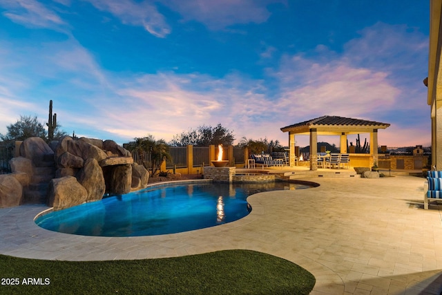 pool at dusk with a gazebo, fence, a pool with connected hot tub, and a patio