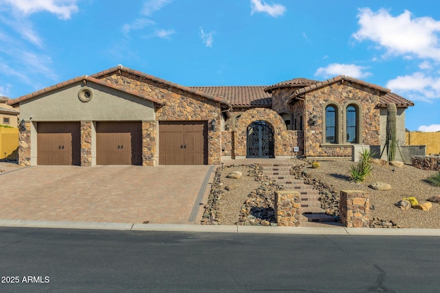 mediterranean / spanish-style home with stucco siding, a garage, stone siding, a tile roof, and decorative driveway