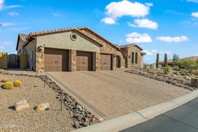 mediterranean / spanish home featuring stucco siding, a gate, decorative driveway, stone siding, and an attached garage