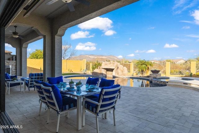 view of patio featuring outdoor dining area, a mountain view, a fenced backyard, and a ceiling fan