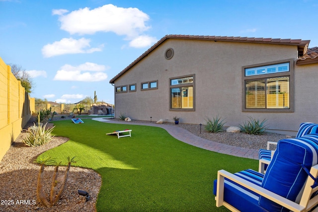 back of property with stucco siding, a lawn, a tile roof, and fence