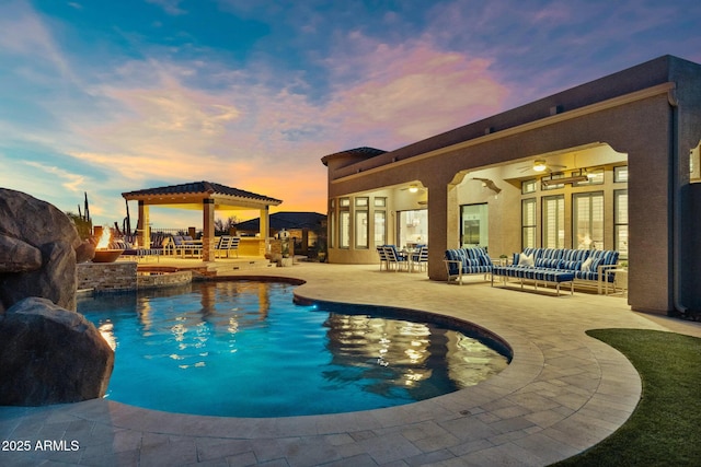 pool at dusk with a patio, a pool with connected hot tub, and an outdoor hangout area