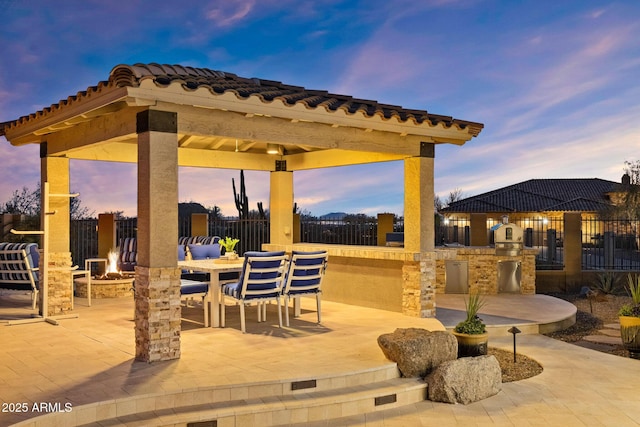 view of patio / terrace with an outdoor kitchen, a gazebo, fence, and a fire pit