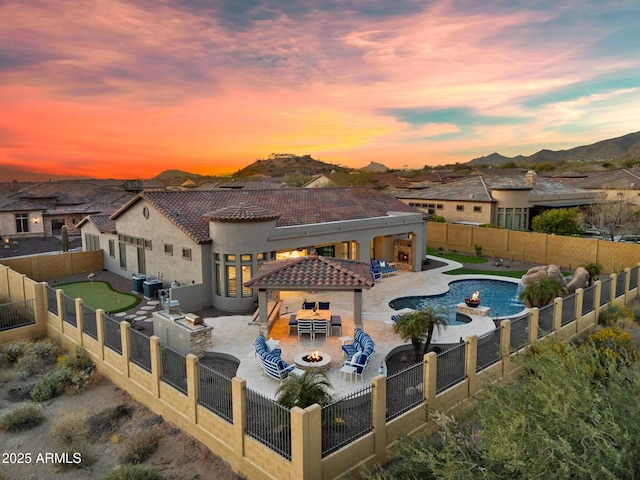 back of property at dusk featuring exterior kitchen, a patio, a fenced backyard, and a tile roof