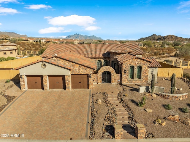 mediterranean / spanish house with a mountain view, a tile roof, decorative driveway, and an attached garage