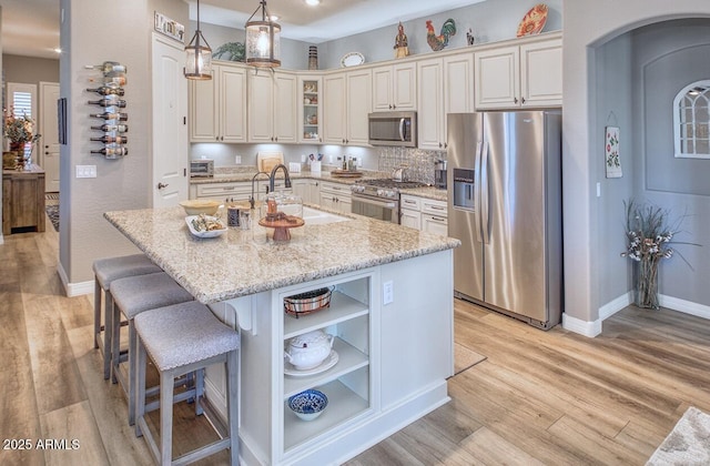 kitchen with pendant lighting, appliances with stainless steel finishes, light stone countertops, light hardwood / wood-style floors, and a center island with sink