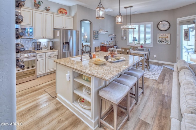 kitchen with light hardwood / wood-style flooring, hanging light fixtures, stainless steel appliances, light stone counters, and an island with sink