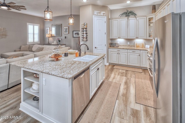 kitchen with appliances with stainless steel finishes, sink, hanging light fixtures, light stone counters, and a center island with sink