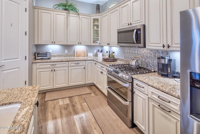 kitchen featuring appliances with stainless steel finishes, tasteful backsplash, white cabinets, light stone countertops, and light wood-type flooring