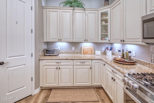 kitchen with light stone counters, stainless steel appliances, light hardwood / wood-style flooring, and white cabinets