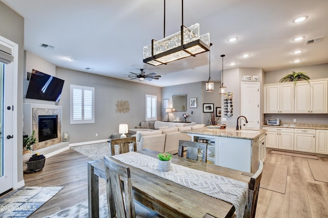 dining area with sink, a fireplace, ceiling fan, and light wood-type flooring