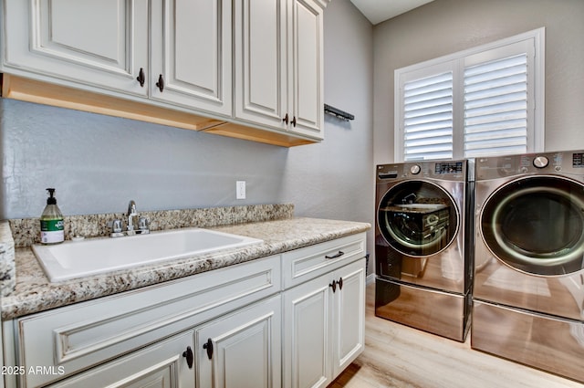 clothes washing area featuring sink, light hardwood / wood-style flooring, cabinets, and washing machine and clothes dryer