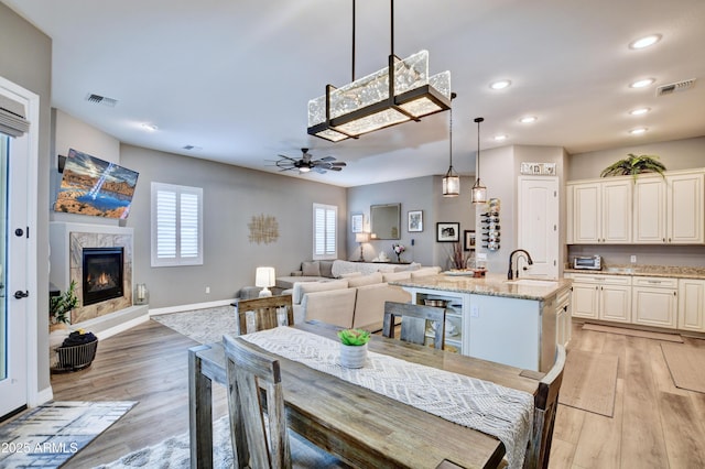 dining area with sink, a premium fireplace, ceiling fan, and light wood-type flooring