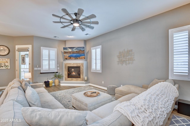 living room featuring a premium fireplace, wood-type flooring, and ceiling fan