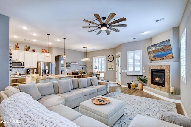 living room with ceiling fan, a high end fireplace, and light hardwood / wood-style floors