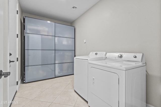 clothes washing area featuring washer and dryer, visible vents, laundry area, and light tile patterned floors