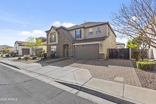 traditional-style house with stucco siding, decorative driveway, stone siding, fence, and a garage