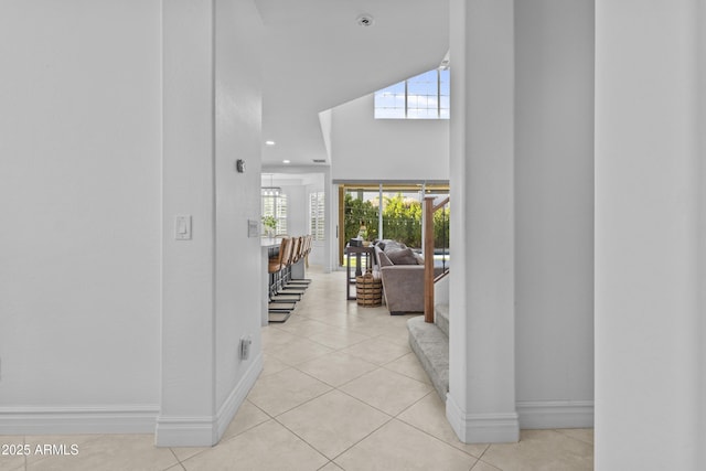 hallway with a high ceiling, light tile patterned floors, recessed lighting, and baseboards