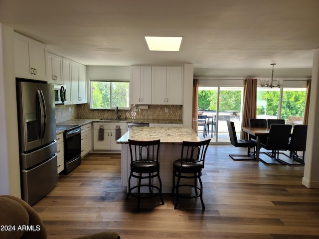 kitchen with white cabinetry, stainless steel appliances, light stone counters, a kitchen island, and decorative light fixtures