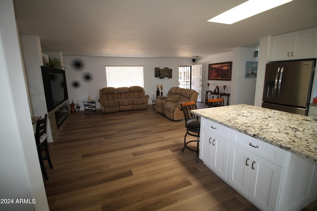 kitchen featuring stainless steel refrigerator with ice dispenser, a breakfast bar area, white cabinetry, dark hardwood / wood-style flooring, and light stone countertops