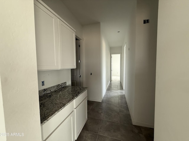 corridor featuring baseboards and dark tile patterned flooring