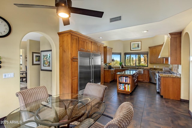 kitchen featuring sink, high quality appliances, a kitchen island, ceiling fan, and wall chimney range hood