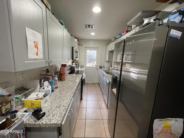 kitchen with light tile patterned floors, appliances with stainless steel finishes, white cabinetry, and light stone countertops