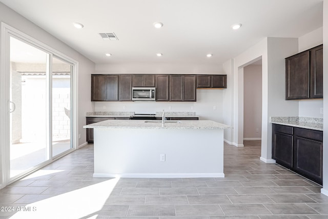 kitchen featuring a healthy amount of sunlight, dark brown cabinets, sink, and a kitchen island with sink