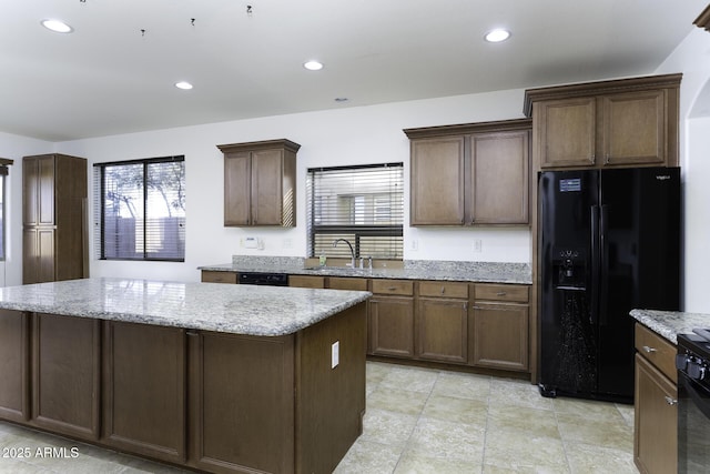 kitchen featuring light stone countertops, dark brown cabinets, sink, black appliances, and a kitchen island