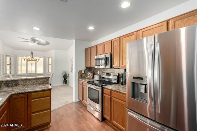 kitchen with appliances with stainless steel finishes, tasteful backsplash, dark stone counters, hanging light fixtures, and light wood-type flooring